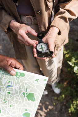 Cropped view of african american man holding map near senior wife with compass  clipart