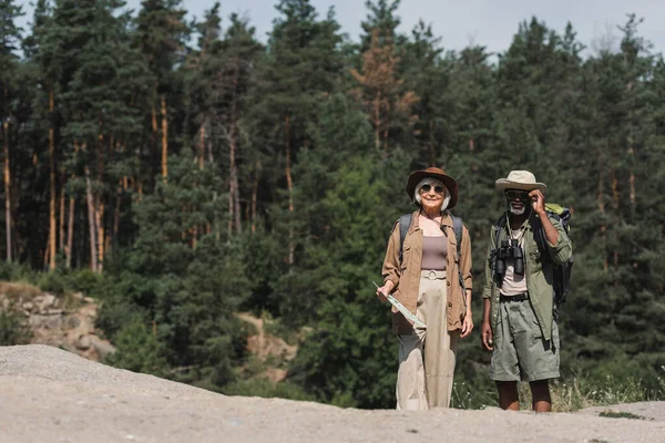 Usmívající Starší Turista Drží Mapu Blízkosti Afrického Amerického Manžela Skále — Stock fotografie