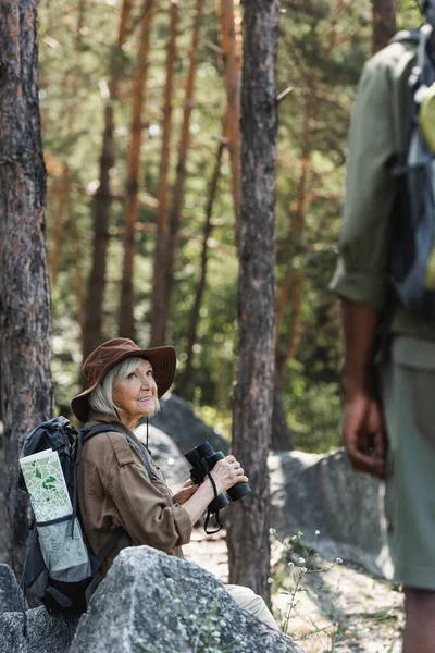 Smiling Senior Woman Holding Binoculars Blurred African American Husband Forest — ストック写真