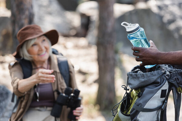 Африканский американец держит бутылку воды рядом с размытой женой в лесу 