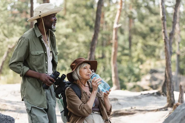 Turista Afroamericano Sosteniendo Prismáticos Cerca Esposa Mayor Con Agua Bosque — Foto de Stock