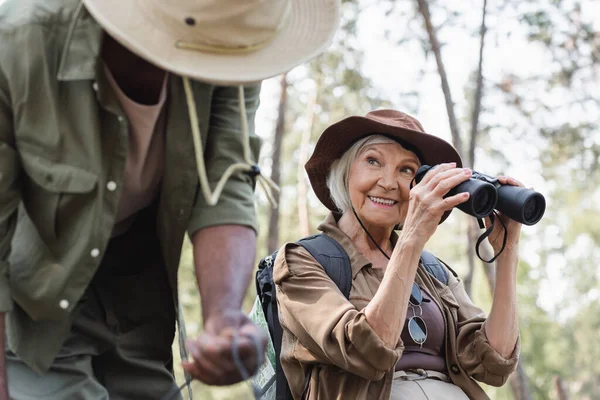 Senior Traveler Holding Binoculars Blurred African American Husband Forest — Stock Photo, Image