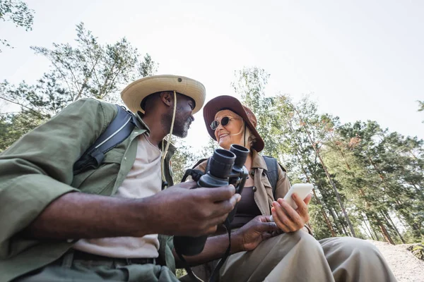 Nízký Úhel Pohledu Pozitivních Multietnických Turistů Držících Smartphone Dalekohled Lese — Stock fotografie