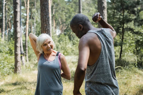 Mujer Mayor Sonriendo Mientras Hace Ejercicio Con Marido Afroamericano Bosque — Foto de Stock