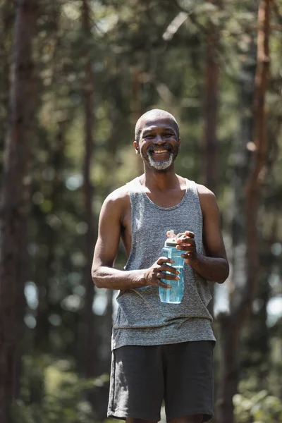 夏の森の中でスポーツボトルを保持するシニアアフリカ系アメリカ人スポーツマン — ストック写真