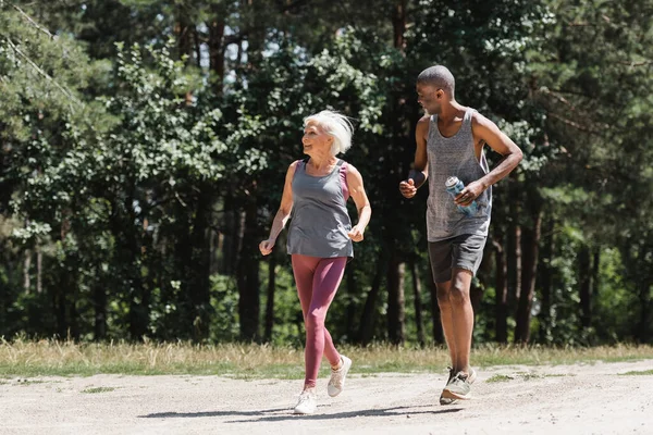 Smiling Senior Sportswoman Jogging African American Husband Sports Bottle Forest — Stock Photo, Image