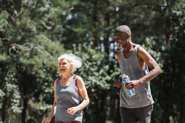 Familia Multiétnica Positiva Con Botella Deportiva Corriendo Bosque —  Fotos de Stock