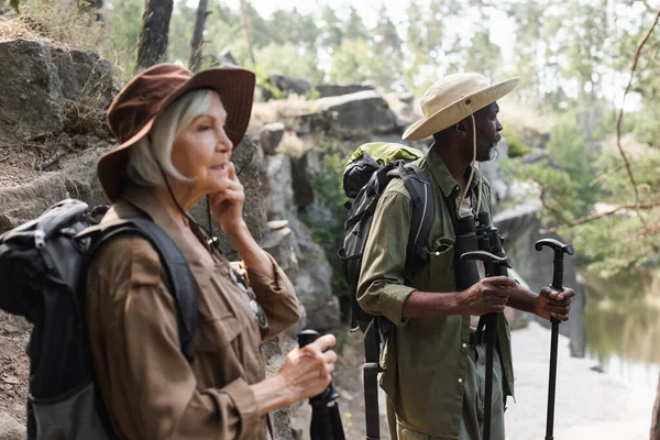 Ormanda bulanık karısının yanında yürüyüş direkleri olan Afrikalı Amerikalı bir turist. 