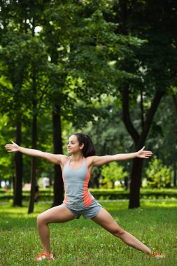full length of cheerful sportswoman with outstretched hands exercising in park clipart