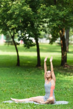 Spor giyim bölümünde formda bir kadın parkta yoga minderinde pratik yapıyor.