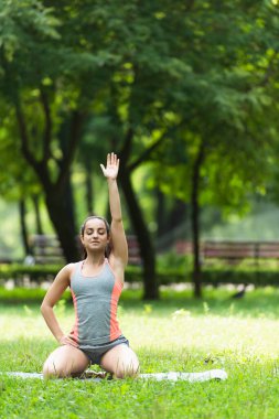 Elleri kalçasında oturan ve yoga minderinde çalışırken elini kaldıran genç bir kadın.