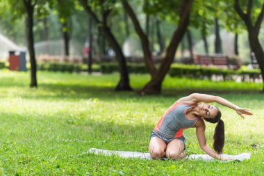 Spor giyim sektöründe esnek bir kadın parkta yoga minderinde esniyor.