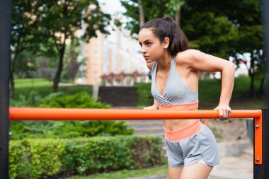 focused woman in sportswear exercising on parallel bars outside clipart