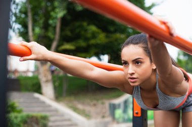 Spor giyim sektöründe konsantre bir kadın dışarıda paralel barlarda egzersiz yapıyor.