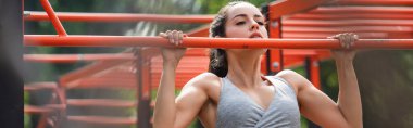 Genç atletik kadın açık hava spor salonunda barfiks çekiyor.