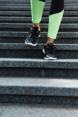 partial view of sportive woman running on stairs outside  clipart