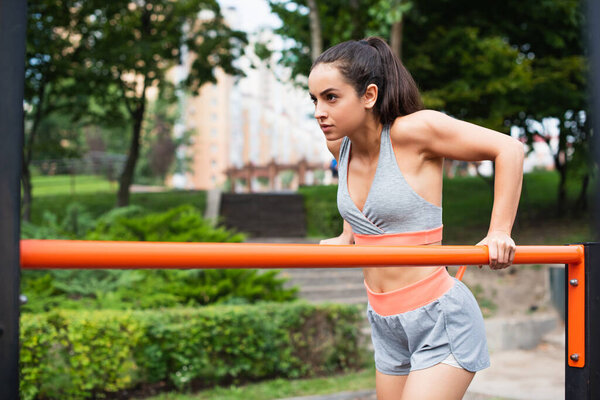 focused woman in sportswear exercising on parallel bars outside