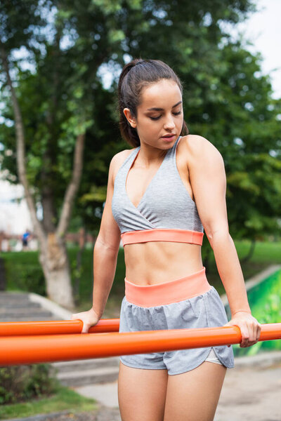 pretty woman in sportswear exercising on parallel bars outside