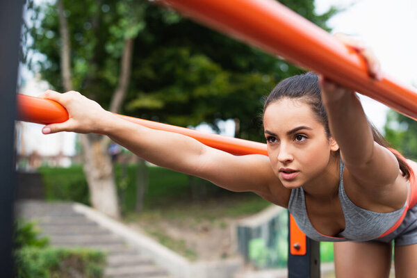 concentrated woman in sportswear exercising on parallel bars outside