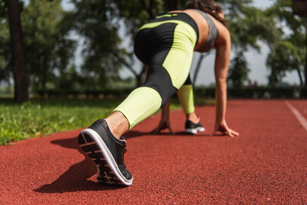 back view of sportswoman in starting pose on stadium 