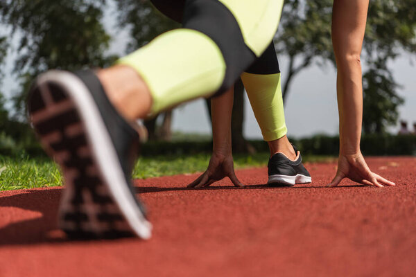 частичный вид спортсменки в стартовой позе на стадионе 