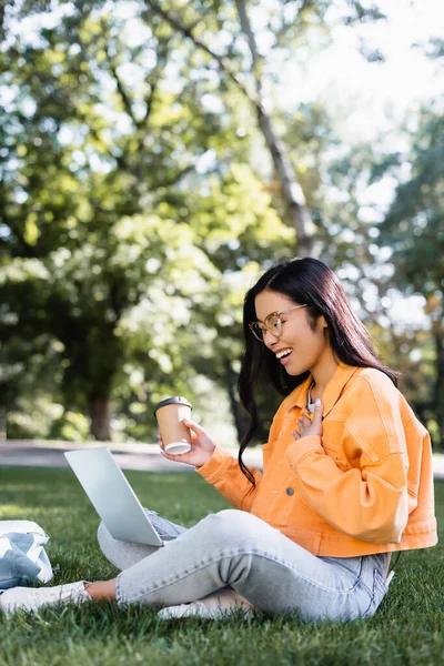 Alegre Asiático Estudante Com Café Para Tocando Peito Enquanto Sentado — Fotografia de Stock