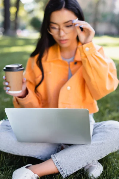 커피를 마시고 아시아인 여인은 노트북을 보면서 안경을 조정하러 — 스톡 사진