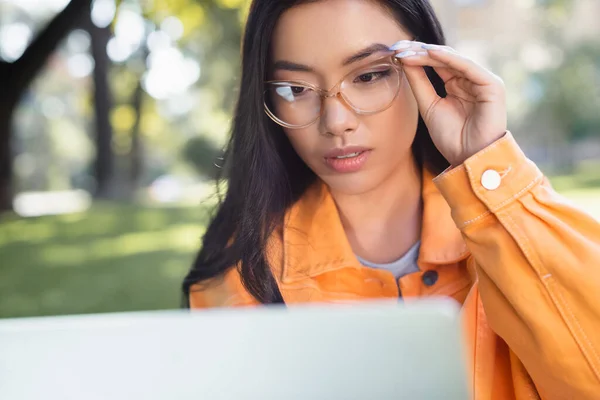 在户外看模糊的笔记本电脑时 体贴的亚洲女人摸着眼镜 — 图库照片