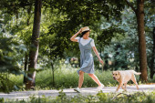 young asian woman in sundress and straw hat running with dog in park