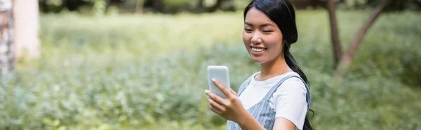 快乐的亚洲女人在公园里用手机聊天 挂着横幅 — 图库照片