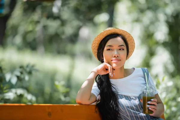 Marzycielka Uśmiechnięta Azjatka Słomkowym Kapeluszu Siedząca Świeżym Smoothie Parku — Zdjęcie stockowe