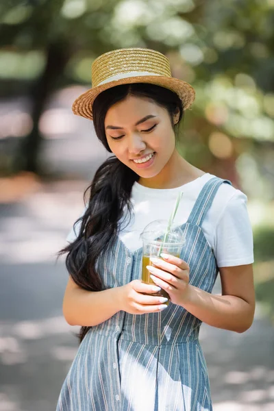 屋外で立ちながら生ジュースのプラスチックカップを持っているアジアの女性を喜んで — ストック写真