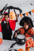 afro-amerikai gyerek halloween jelmezben boszorkány üstöt tart bájitallal közeli testvér játék pók