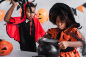 afro-amerikai lány halloween jelmezben boszorkány üstöt tart bájitallal közeli testvér játék pók