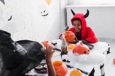 Cadılar Bayramı kostümlü mutlu Afro-Amerikalı çocuk sivri uçlu şapkalı, balkabağı oyulmuş kız kardeşinin yanında.