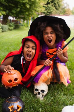 spooky african american kids in halloween costumes screaming while playing on backyard clipart