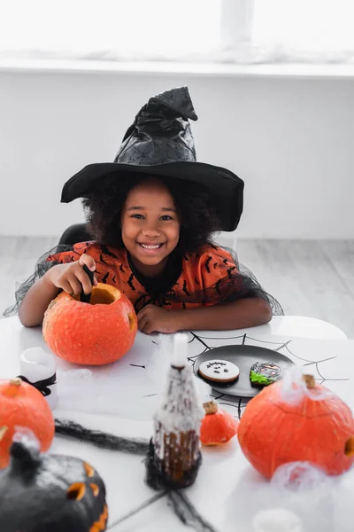Happy African American Girl Witch Halloween Costume Carving Pumpkin Cookies — Stock Photo, Image