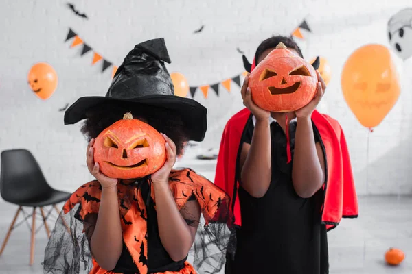 Niños Afroamericanos Disfraces Halloween Cubriendo Caras Con Calabazas Talladas Casa —  Fotos de Stock