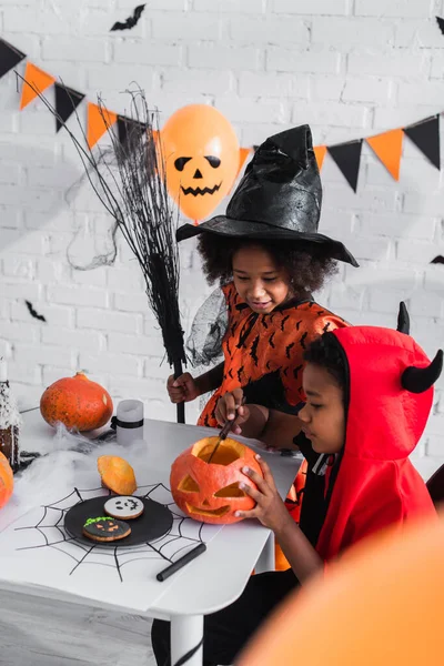 Africký Americký Chlapec Halloween Kostým Vyřezávání Dýně Poblíž Sestra Koštětem — Stock fotografie