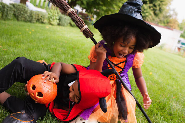 african american siblings in halloween costumes screaming while playing on backyard