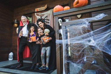 Cadılar Bayramı süsüsüyle verandada gülen ürkütücü kostümlü neşeli bir aile.