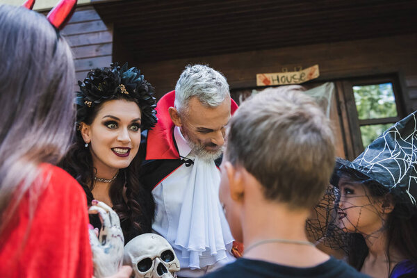 Жуткая женщина в костюме Хэллоуина держит череп и гримасничает рядом с семьей