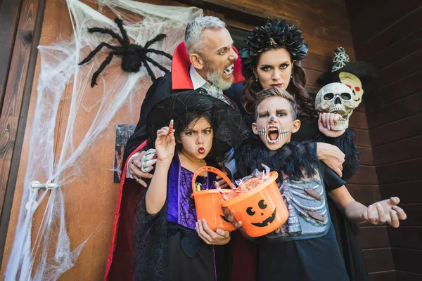 Família Trajes Assustadores Sorrir Perto Porta Com Decoração Halloween — Fotografia de Stock