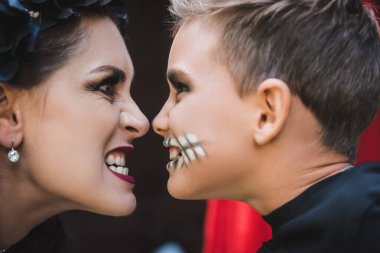 side view of mother and son in spooky makeup grinning at each other clipart