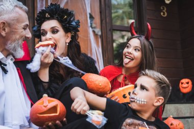 woman eating raw pumpkin near excited family in spooky halloween costumes