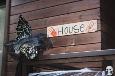 spooky skull in witch hat with black veil near blurred card with house lettering and bloody hand prints clipart