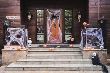 entrance of cottage decorated with carved pumpkins, spider net, toy spiders and paper cut bats clipart