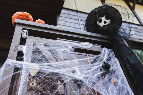 low angle view of carved pumpkins and scarecrow in witch hat on porch fence decorated with spider net