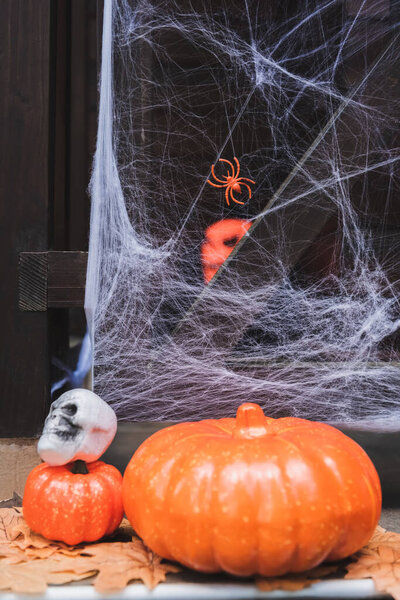 orange pumpkins and spooky skull on porch decorated with spider net
