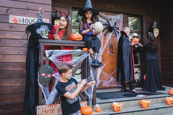 Rodina Halloween Kostýmy Zdobení Veranda Dřevěné Chalupy Děsivými Atributy — Stock fotografie